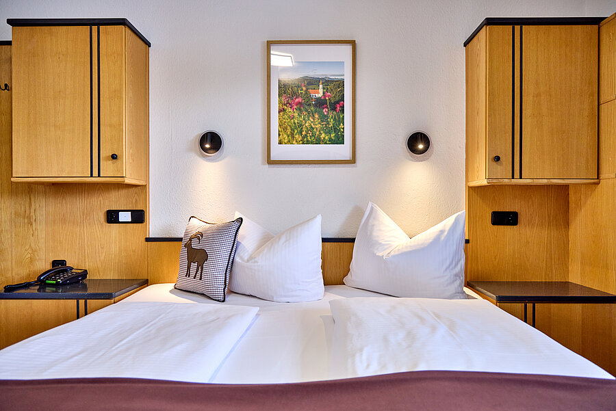 Detailaufnahme des Doppelbetts, das beidseitig von Hängeschränken eingefasst ist. Darüber befinden sich zwei Leuchten und ein Landschaftsbild. 