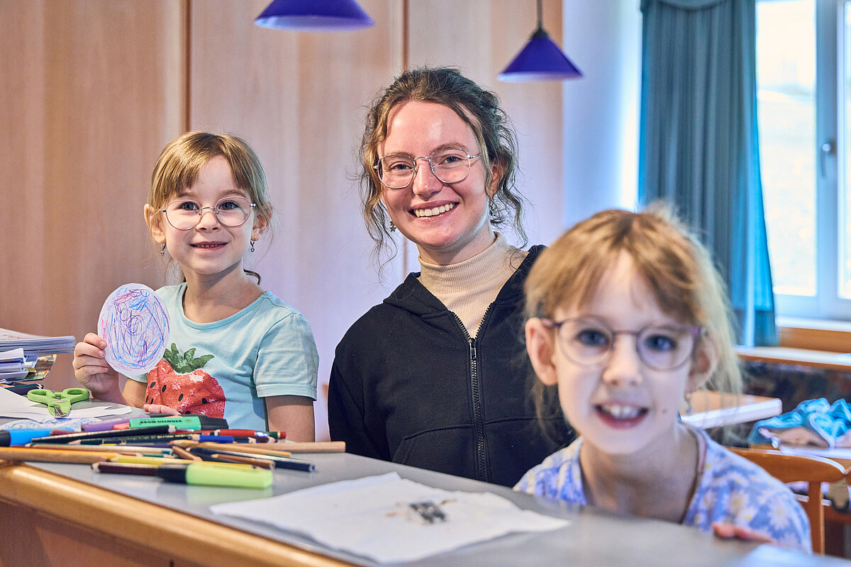 Fröhliche Malrunde mit zwei Mädchen und einer Mitarbeiterin aus dem Team der Gästebetreuung.