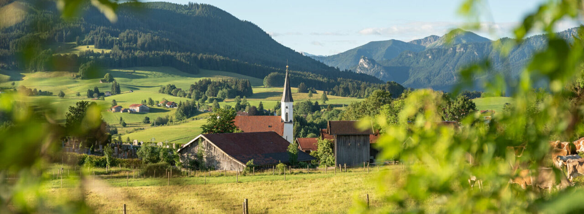 Ein bergliches Landschaftsfoto mit einem kleinem Dorf und einer prominenten Kirche.