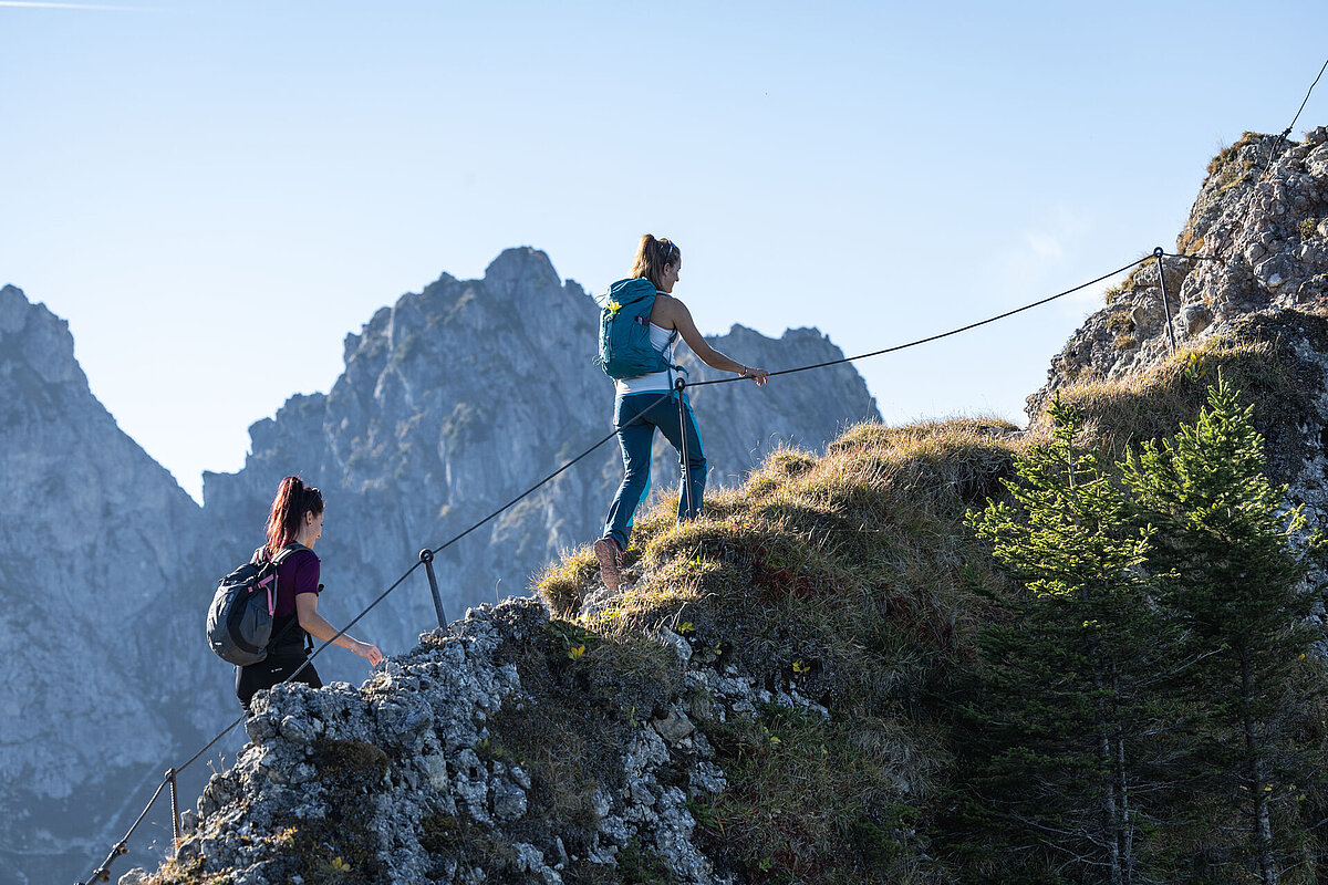 Zwei Bergwanderinnen erklimmen am Drahtseil die letzten Meter bis zum Gipfel.