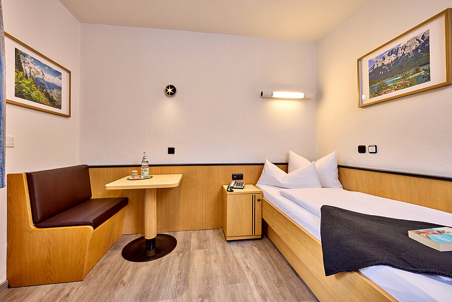 Links neben dem Einzelbett befindet sich eine Einbausitzbank mit hochwertigem Kunstleder und einem quadratischen Tisch.