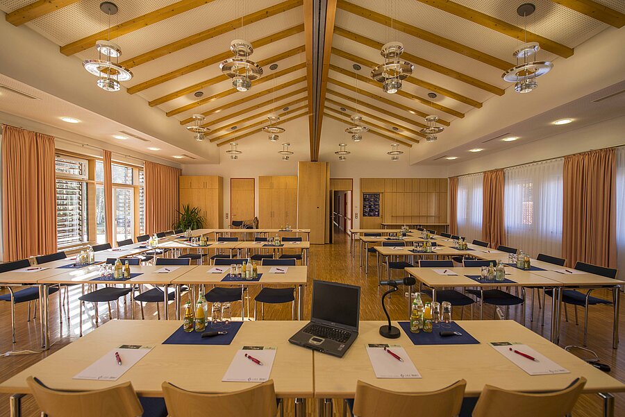 Der hohe Tagungsraum mit Spitzgiebel ist für ein Seminar mit Blöcken, Stiften und Seminargetränken vorbereitet.