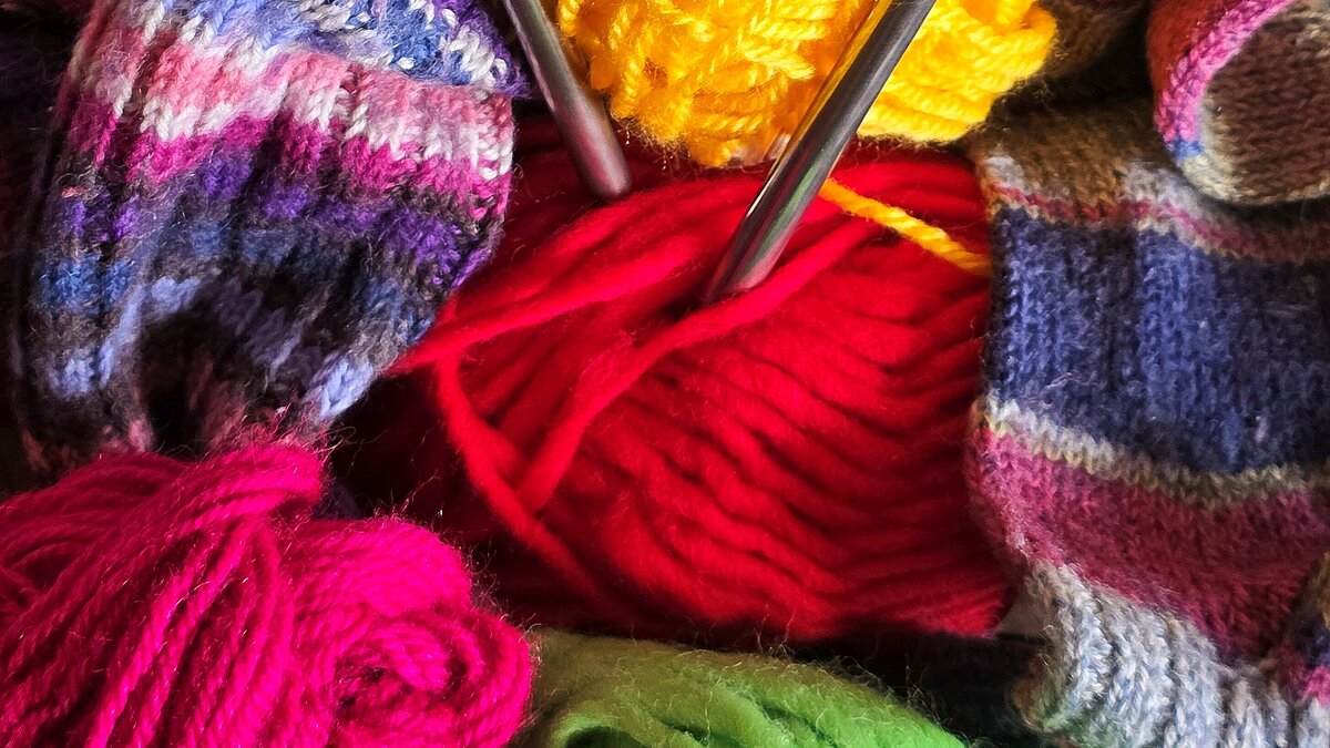 Bunte Wollknäuel und Stricknadeln warten zum Loslegen.