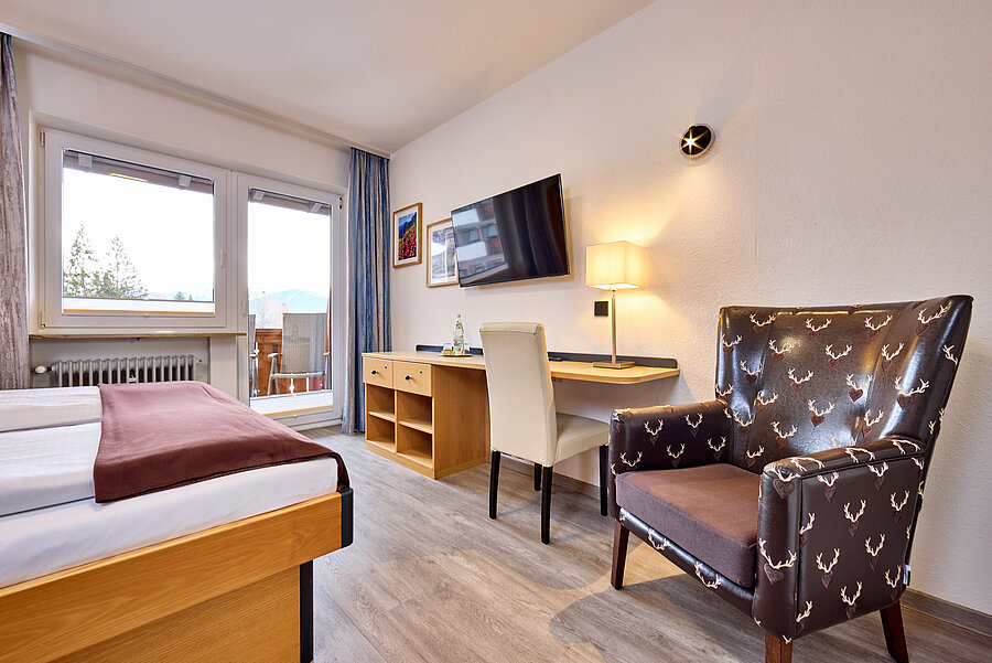 Der stylische Lederstuhl gegenüber des Betts ist mit Hirschköpfen bestickt - daneben befindet sich ein großzügig Schreibtisch und TV-Gerät an der Wand.
