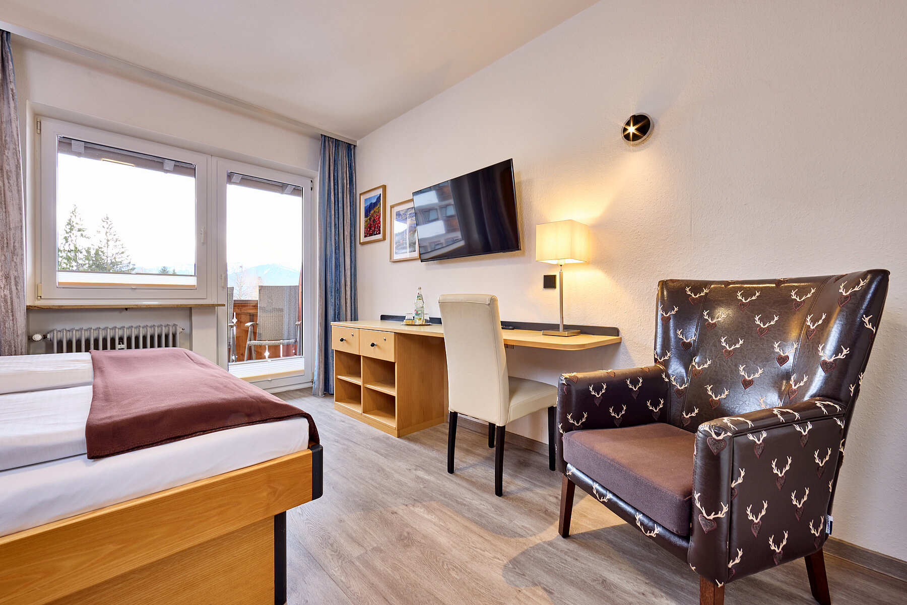 Der stylische Lederstuhl gegenüber des Betts ist mit Hirschköpfen bestickt - daneben befindet sich ein großzügig Schreibtisch und TV-Gerät an der Wand.