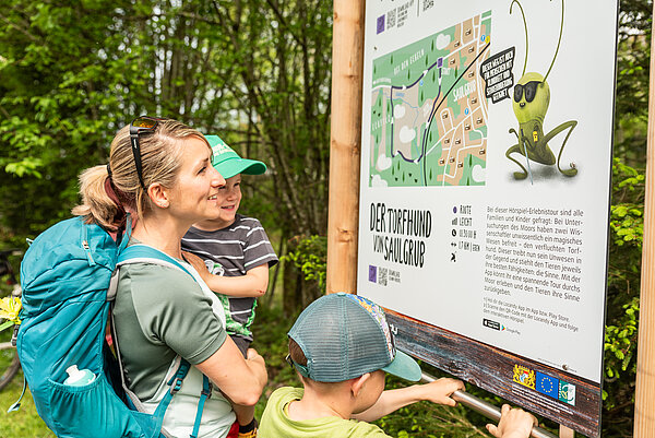 Eine Mutter betrachtet mit ihren beiden Kindern die Schautafel zum Saulgruber Sinnesweg.