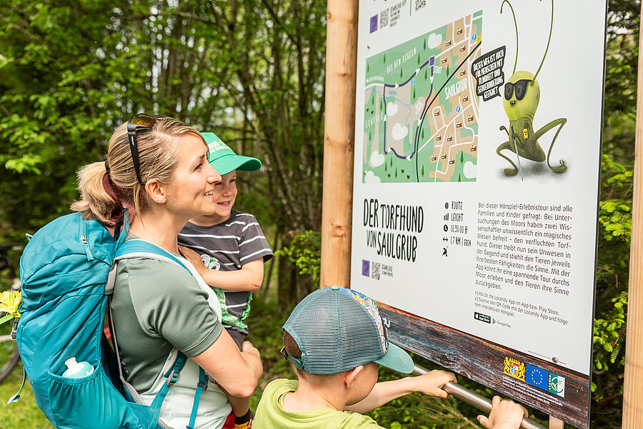 Eine Mutter betrachtet mit ihren beiden Kindern die Schautafel zum Saulgruber Sinnesweg.