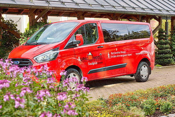Der feuerrote Gästebus parkt neben einem hübschen Blumenbeet am Hoteleingang.