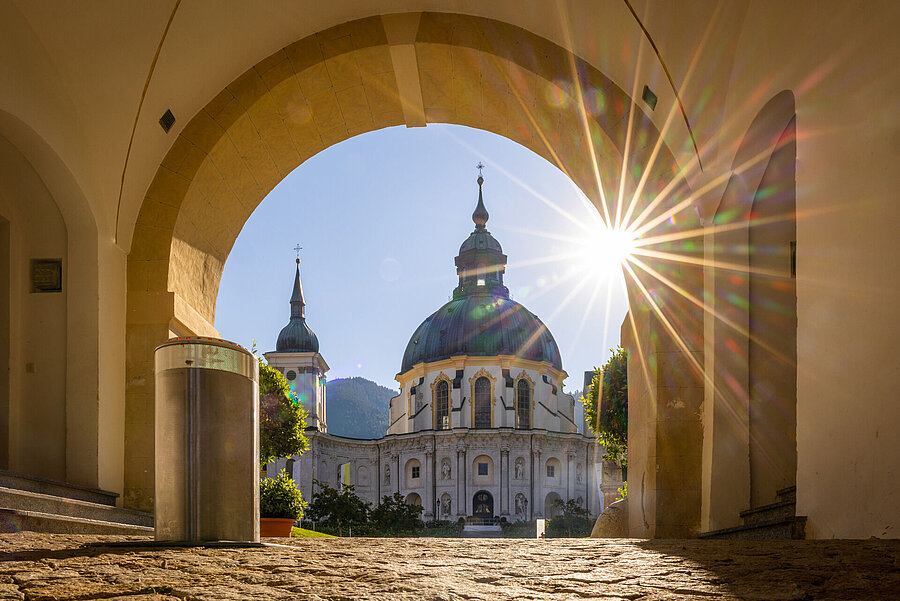 Durch den sonnendurchfluteten Torbogen erblick man die Klosterkirche in Ettal.