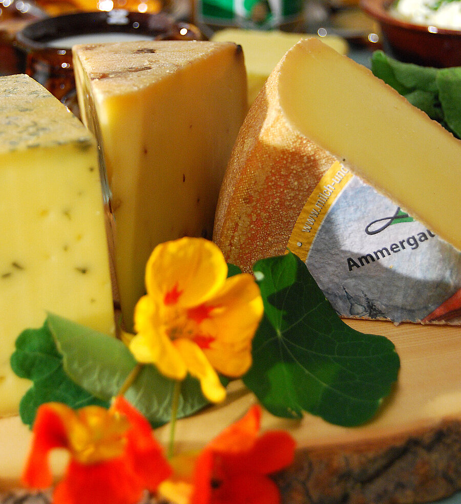 Verschiedene regionale Käsesorten sind hübsch auf einem Brett mit Kapuzinerkresse angerichtet.