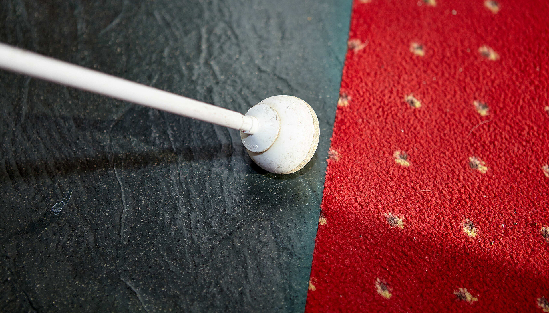 Einen Blindenstock zwischen zwei unterschiedlichen Bodenbelägen