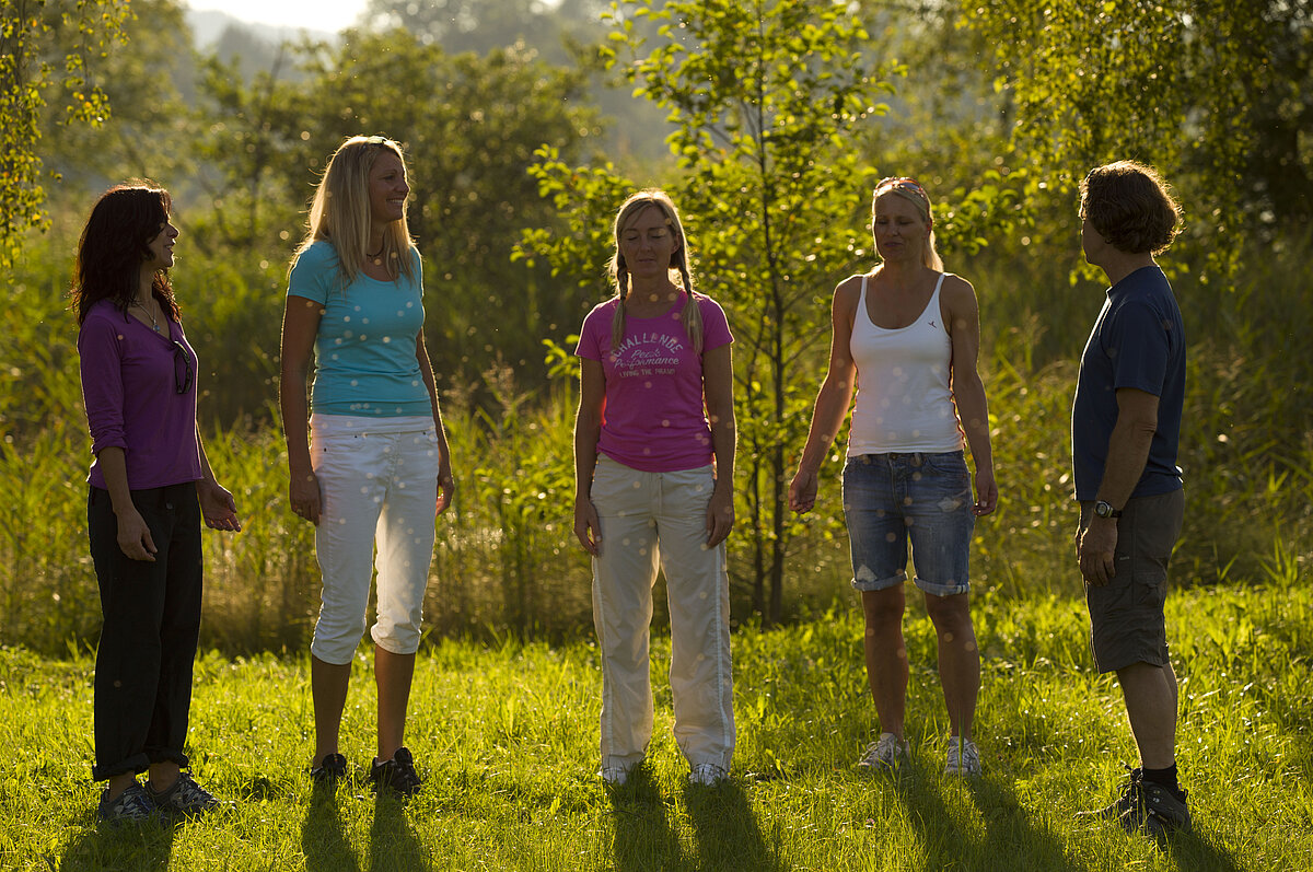 Vier Frauen werden von einem Meditationslehrer in der Natur zu Atemübungen angeleitet.