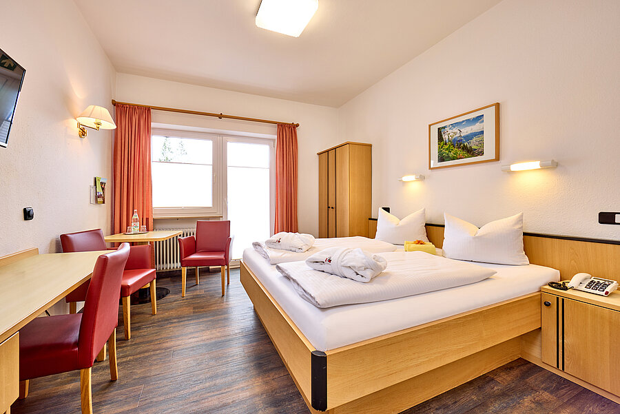 Das Doppelzimmer ist mit hellen Massivholzmöbeln ausgestattet. Rote Kunstledersessel setzen farbige Akzente.