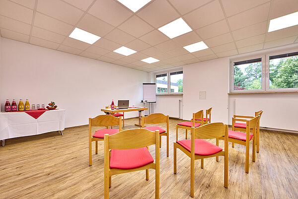 Der Raum Kofel ist mit roten Stühlen ausgestattet und in der Ecke eine Getränkestation mit frischem Obst aufgebaut.