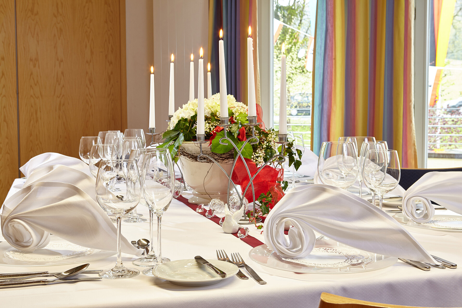 Eine festlich gedeckte Tafel mit Gläsern, Besteck, Kerzen, Blumen und raffiniert gefalteten Stoffservietten lädt zum feiern ein.