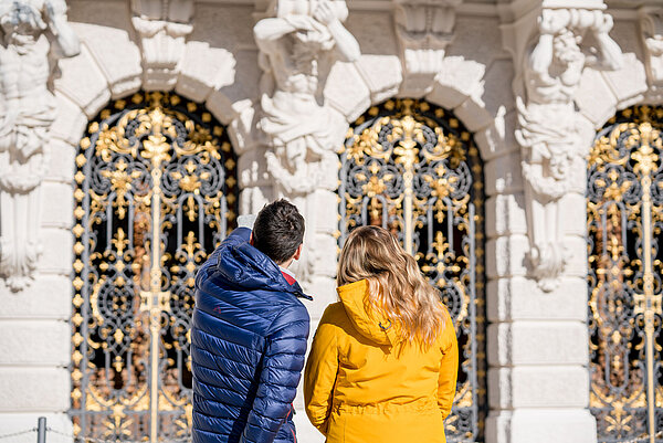 Ein Paar steht vor dem imposanten Schlosseingang und betrachtet die Details.