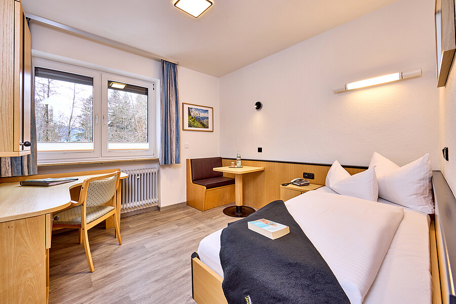 Das großzügige Einzelzimmer verfügt über ein Bett, eine gemütliche Sitzecke und einen separaten Schreibtisch. Helles Licht kommt durch das große Fenster zum Park.