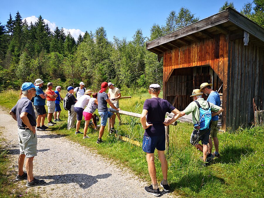 Ein Gruppe Gäste und ehrenamtlicher Begleiter an einem Holzstadl auf dem Saulgruber Sinnesweg. 