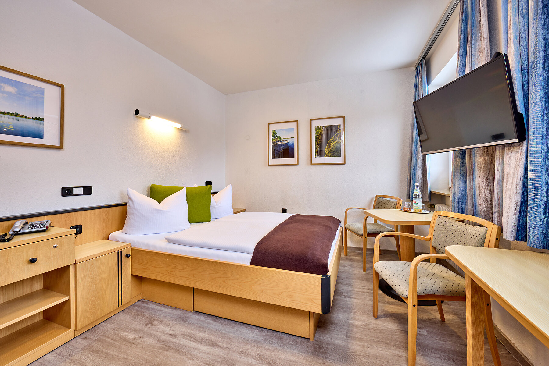 Großzügiges, helles Doppelzimmer mit Bett, Sitzecke und Kommodenkombination zur Ablage.