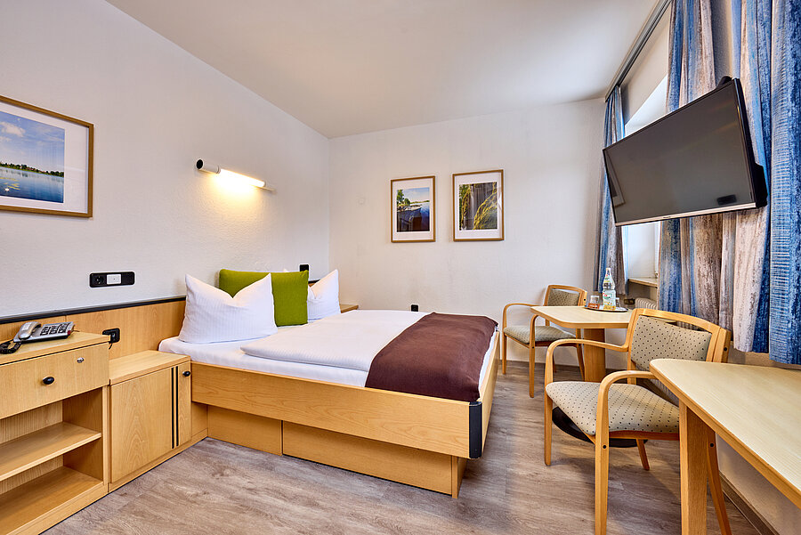 Großzügiges, helles Doppelzimmer mit Bett, Sitzecke und Kommodenkombination zur Ablage.