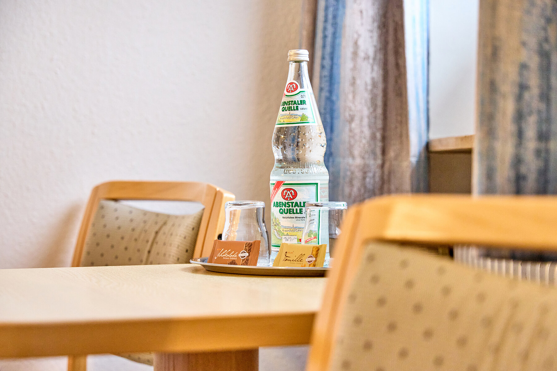 Auf dem hellen Holztisch wartet eine kleine süße Überraschung und eine Flasche Wasser 