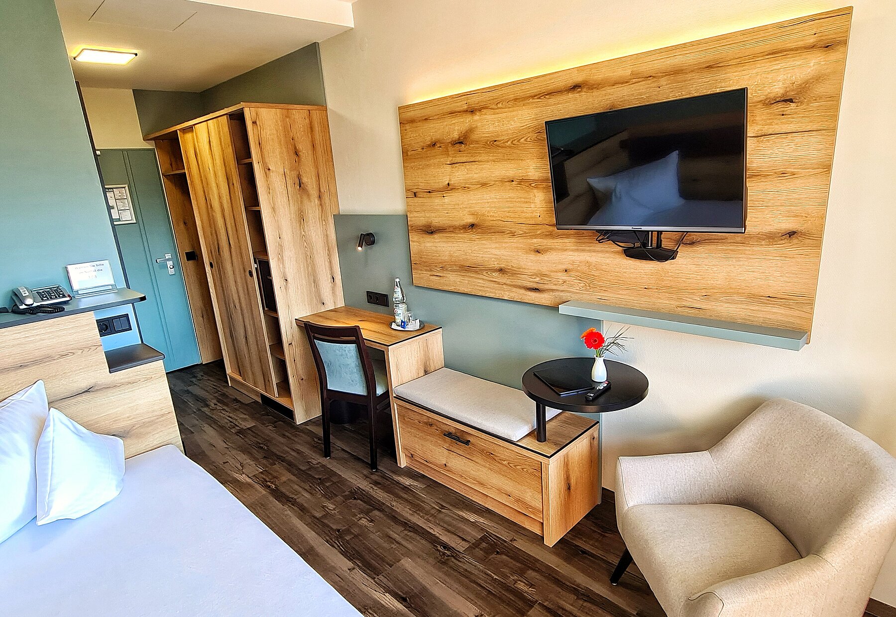 Blick auf Kleiderschrank, Sitzgelegenheiten und TV-Wand - alles in warmen Holztönen