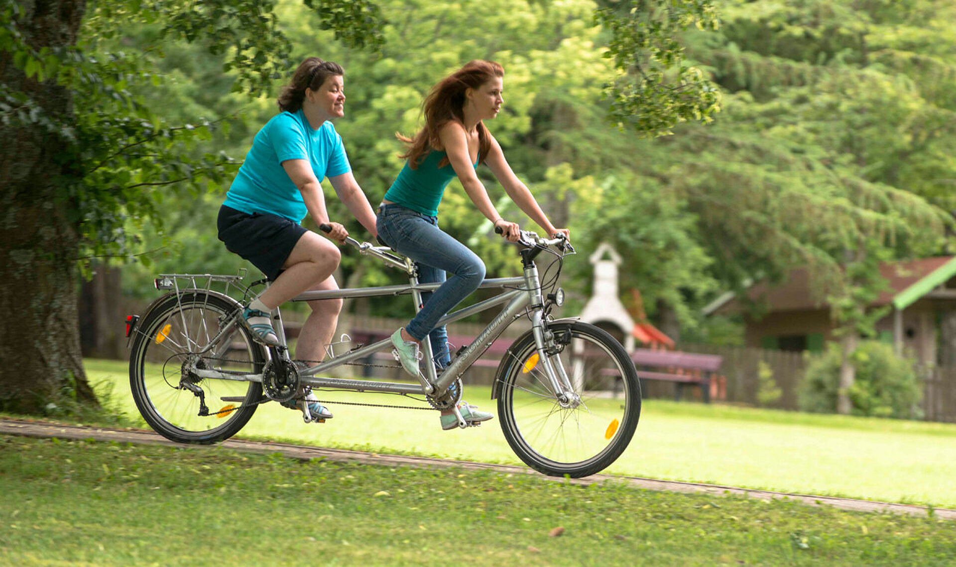 Zwei junge Frauen radeln auf einem Tandem durch den Hotelpark.