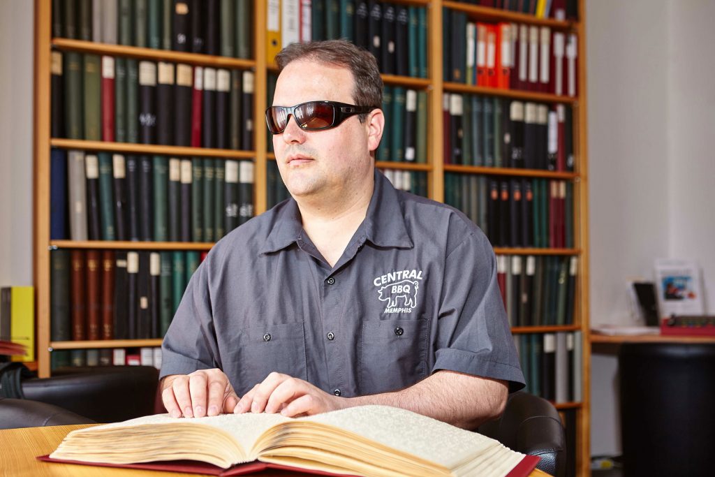 Ein blinder Gast liest ein Brailleschrift-Buch in der Bibliothek