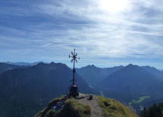 Metallenes Gipfelkreuz vor Gebirgssilhouette und strahlend blauem Himmel