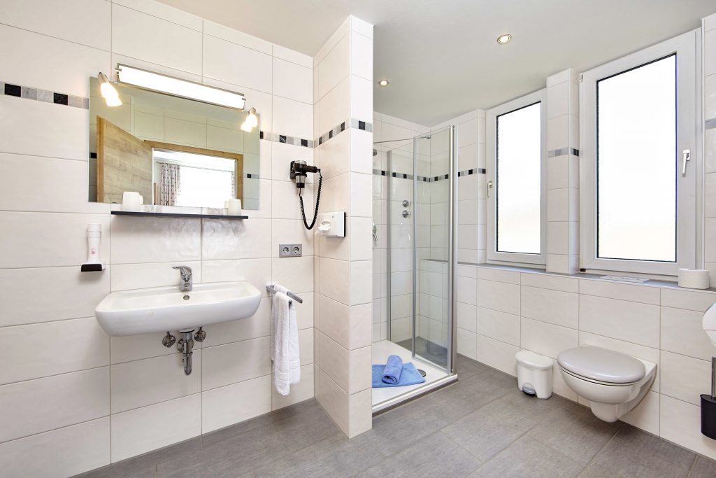 Modernes, helles Bad mit ebenerdiger Dusche, WC, Waschbecken und Spiegel