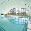 Großes türkises Schwimmbecken in Halle mit großer Fensterfront zum Bergpanorama, Link zu Schwimmbad und Sauna