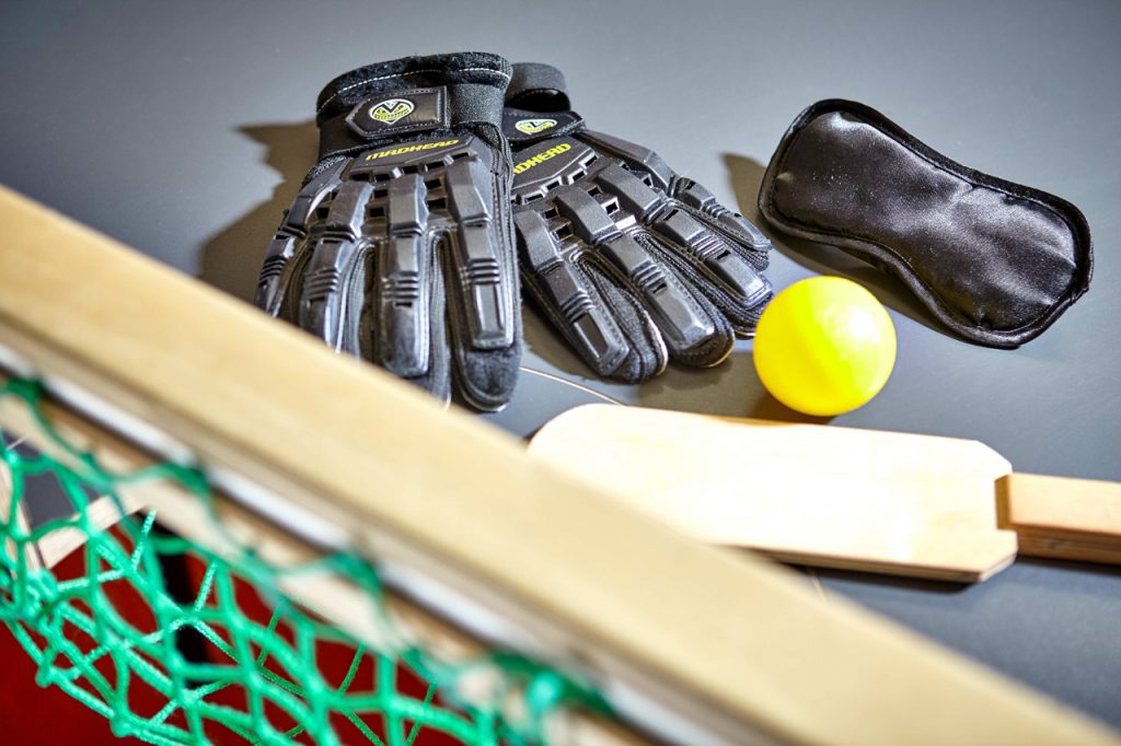 Das Bild zeigt Handschuhe, Augenbinde, Ball und Holzschläger für das Showdownspiel.