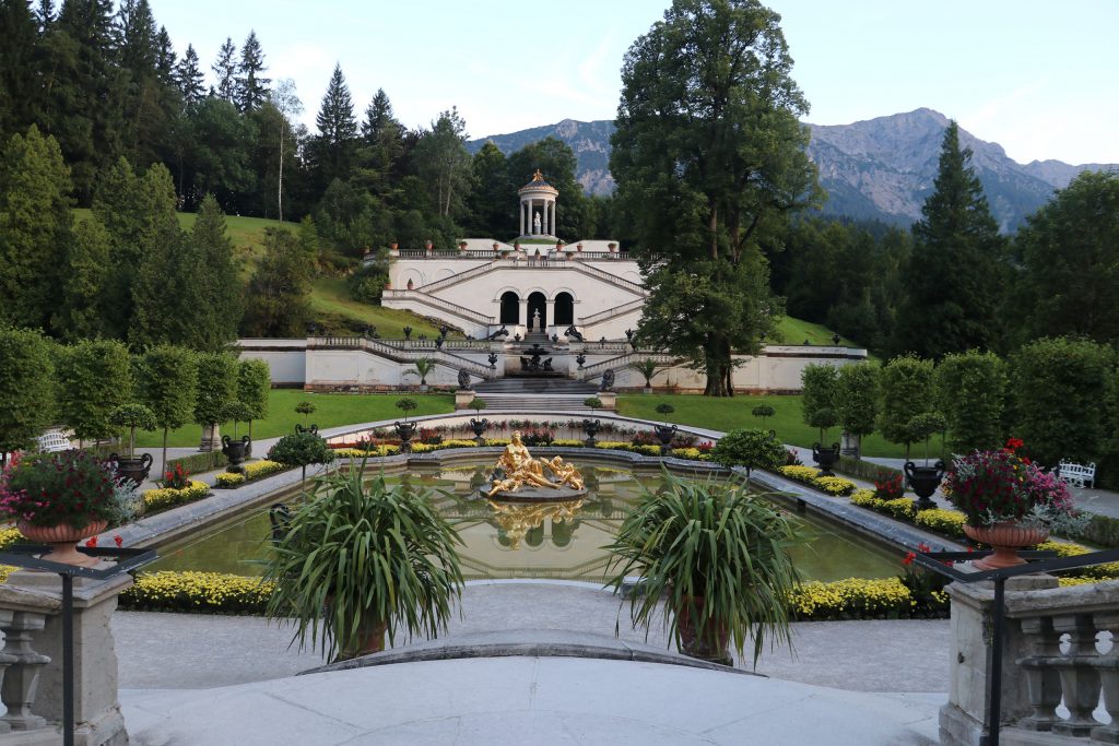 In der Mitte eines kunstvoll gestalteten Gartens befindet sich ein barocker Brunnen mit goldener Figur.
