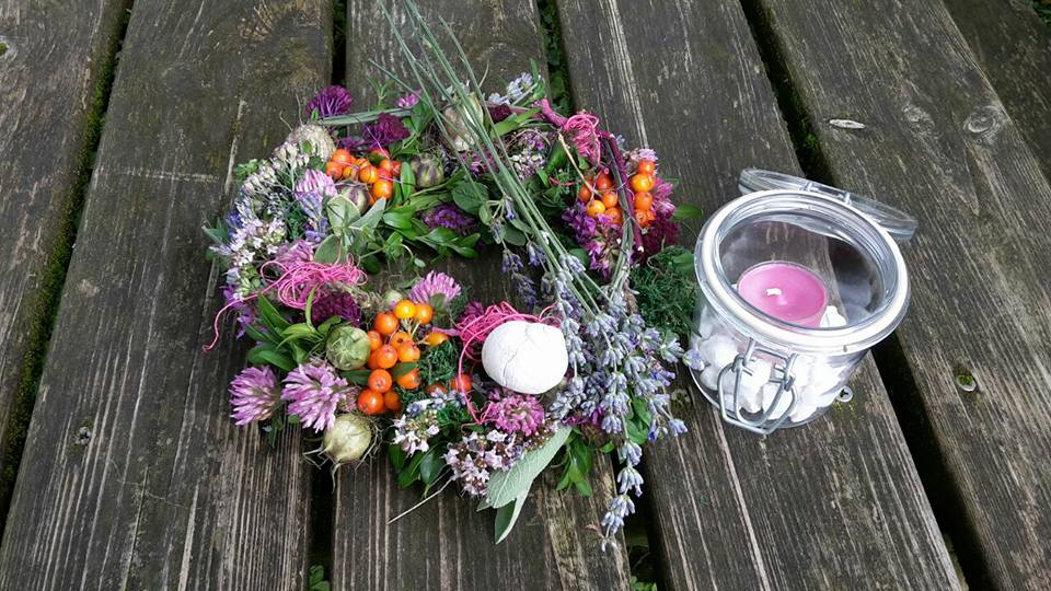 Farbenfroher Blütenkranz mit Klee, Lavendel, verschiedenen Beeren und Windlicht mit Kieselsteinen