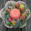 Buntes Blumenarrangement in einem Korb mit oranger Kugelkerze