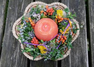 Buntes Blumenarrangement in einem Korb mit oranger Kugelkerze