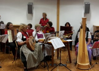 Mitglieder der Camerloher Musikschule musizieren auf verschiedenen Instrumenten, wie Harfe, Zither, Gitarre, Akkordion und Saxophon.