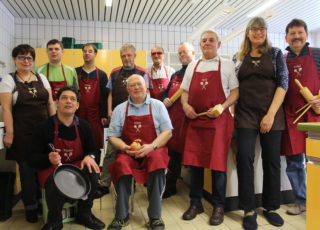 Gruppenfoto des Männer-Kochkurses - alle Herren tragen rote Schürzen.