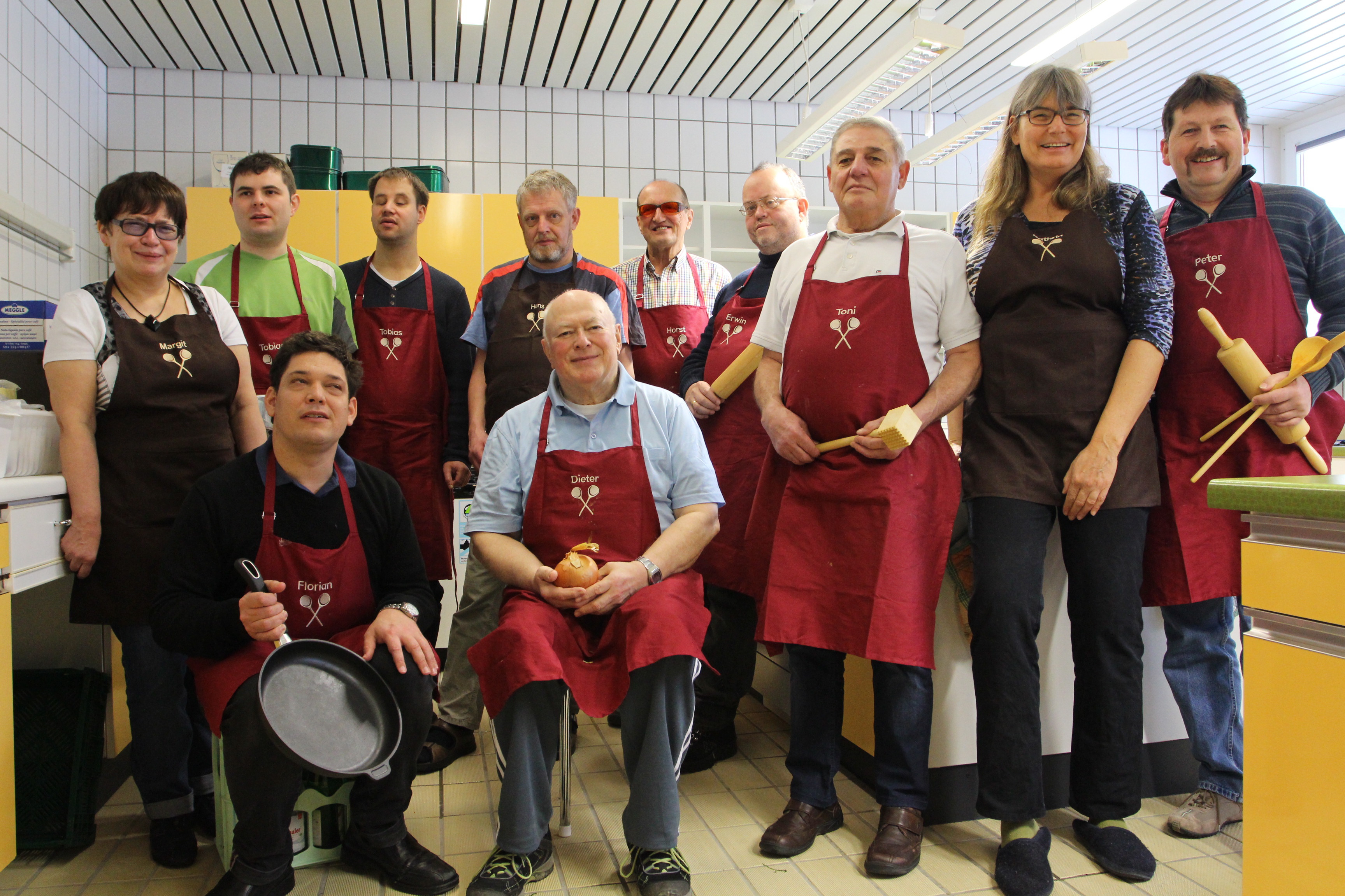 Gruppenfoto des Männer-Kochkurses - alle Herren tragen rote Schürzen.