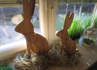 Zwei Hasen aus Holz sitzen im Heu und blicken durch ein Fenster.