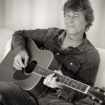 Der Musiker sitzt auf einem Sofa und spielt Gitarre