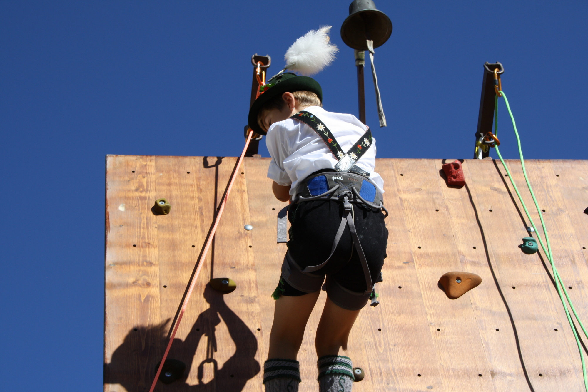 Ein Junge in Tracht und mit Hut erklimmt den oberen Teil eines Kletterturms.