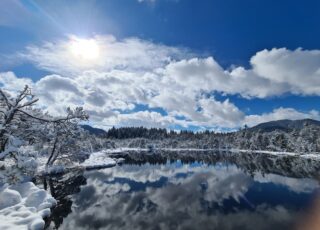 An einem sonnigen Wintertag spiegeln sich die Wolken im tiefblauen Wasser eines kleinen Sees.