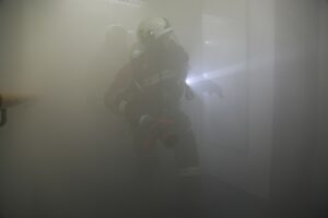 Der Raum ist mit Rauch gefüllt, durch den ein Feuerwehrmann mit Atemschutz eilt.
