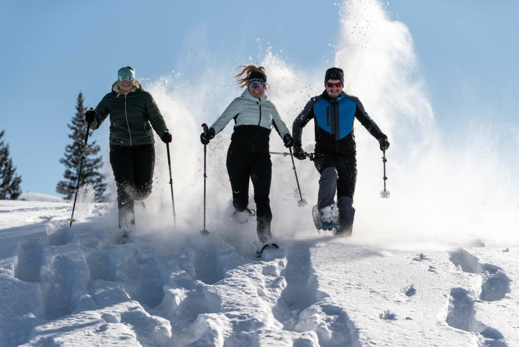 Drei Schneeschuhwanderer laufen fröhlich durch den Schnee