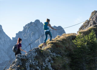 Zwei Wanderinnen gehen am Drahtseil für einen Berggrat