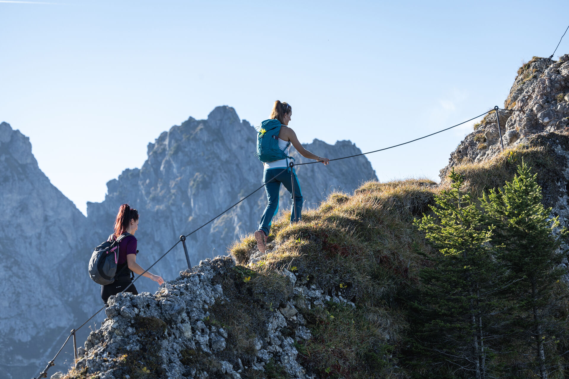 Zwei Wanderinnen gehen am Drahtseil für einen Berggrat