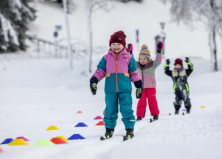 Fröhliche Kinder sammeln erste Erfahrungen auf Skiern